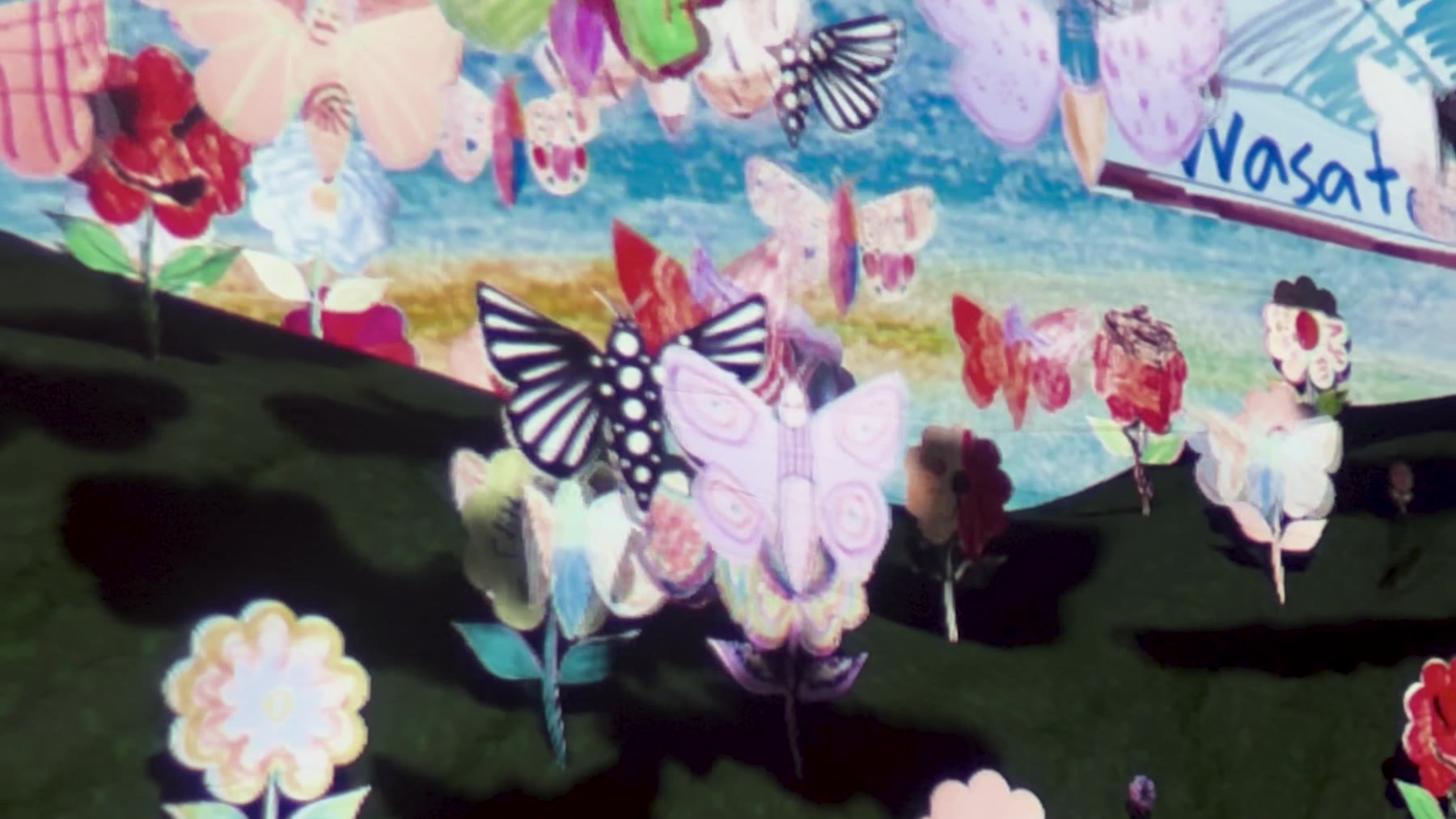 Camera close-up of the projection screen showing a black-and-white polka-dot butterfly, a lavender butterfly, and hand-drawn flowers against the painted sky backdrop, with a billboard reading 'Wasatch...' at right