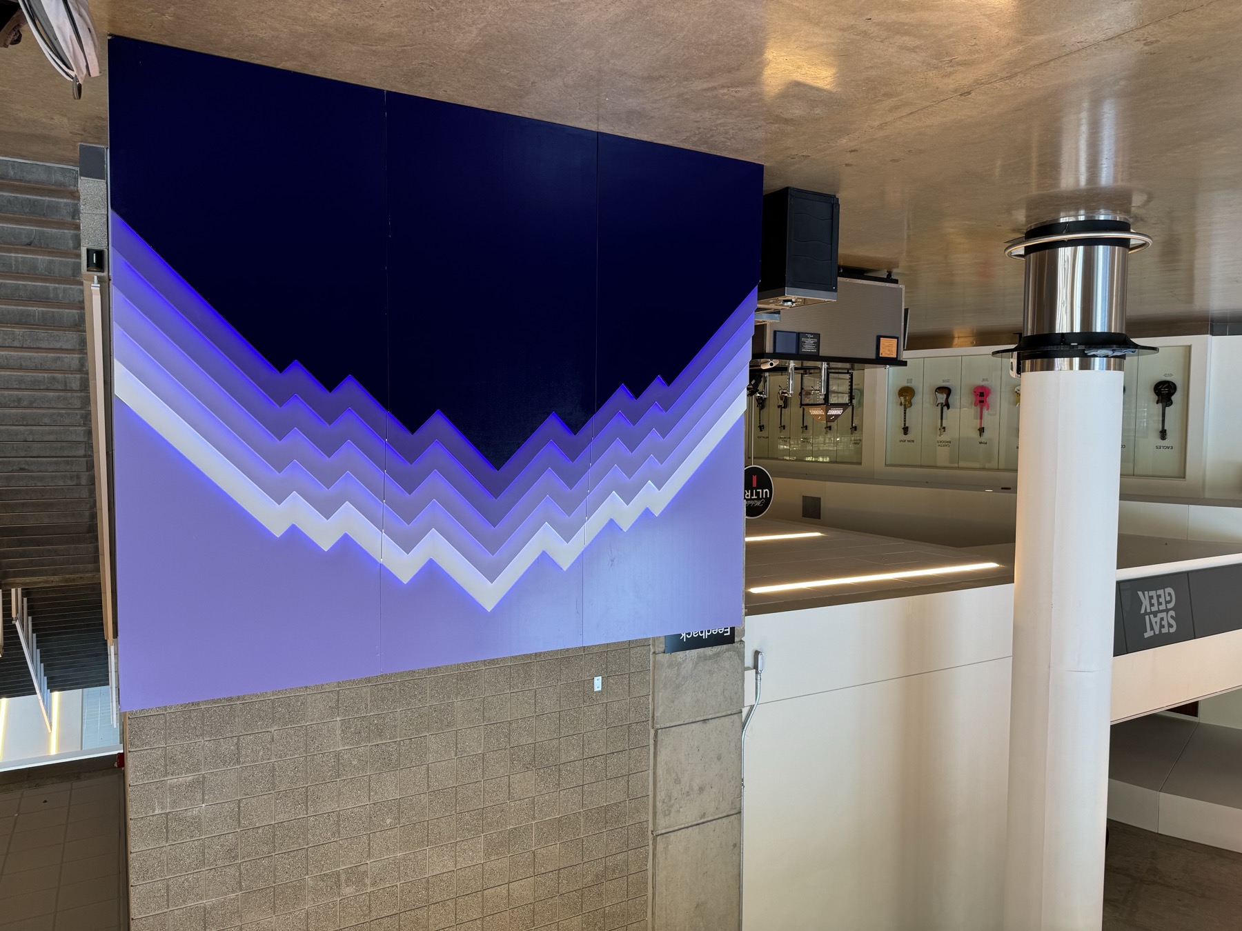 The mountain sculpture unlit in daylight, mounted against a concrete block wall in the arena concourse