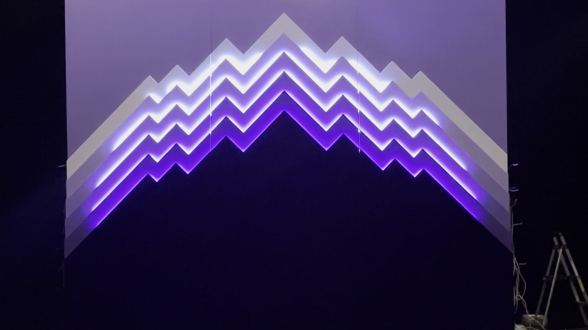 LED sculpture of a stepped mountain skyline, each ridge lit in a white-to-purple gradient, seen straight on with no people in frame