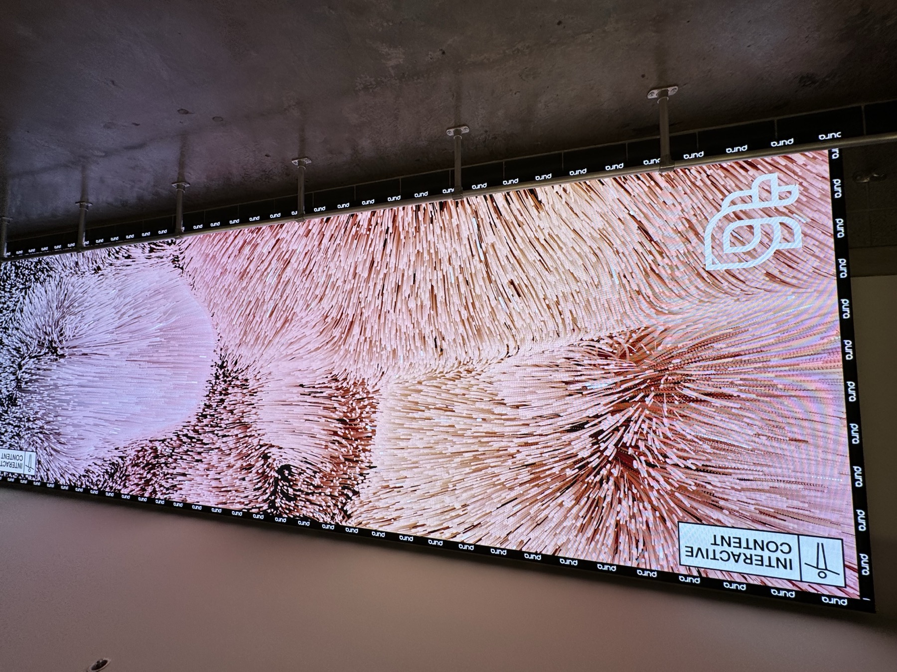 Wide angled view of the wall in its idle Interactive Content state showing the Pura gradient bloom pattern and Pura logo watermark, empty concourse