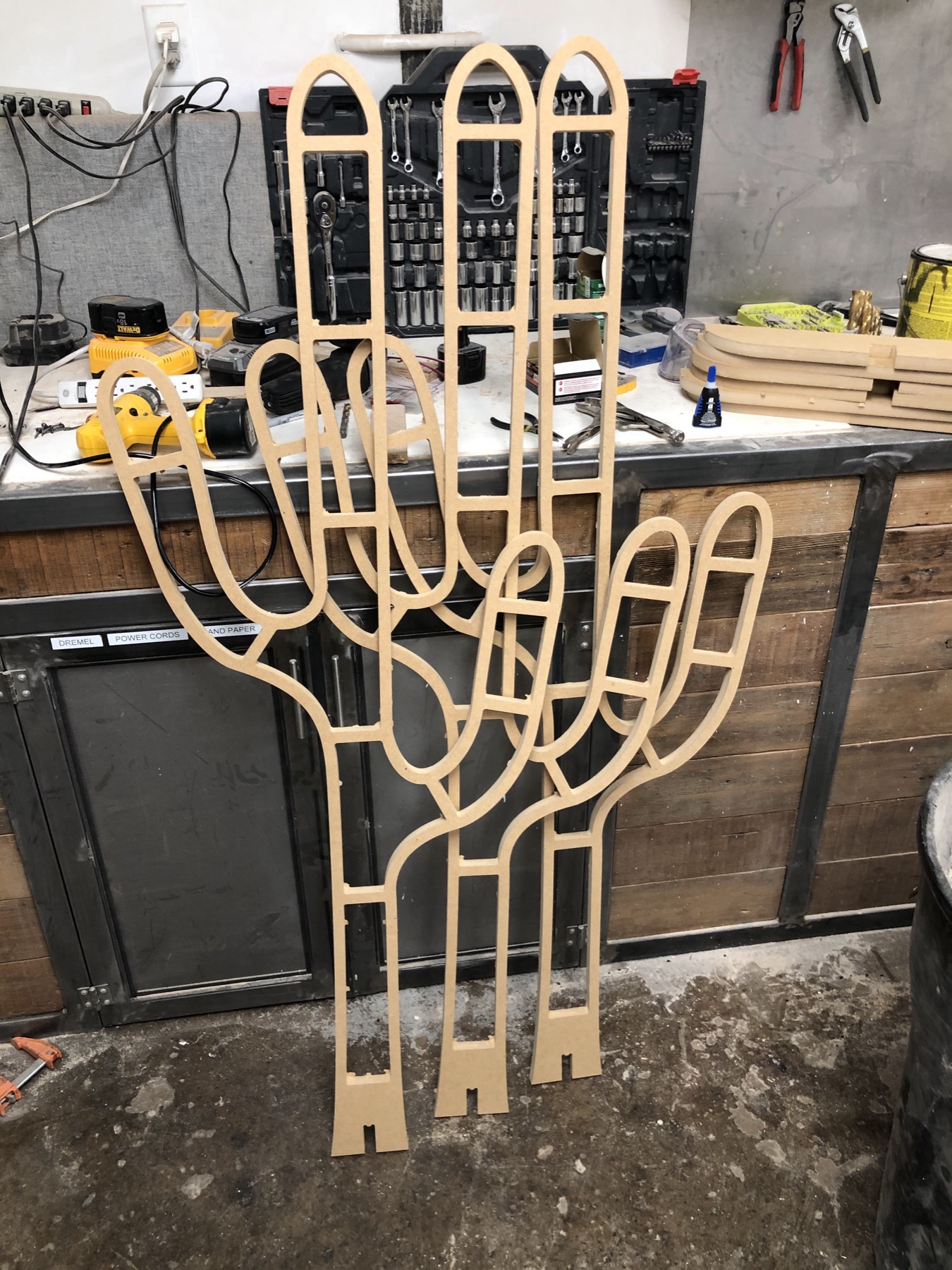 A CNC-cut plywood cactus frame standing in the workshop before paint, with a channel routed around its outline for the LED