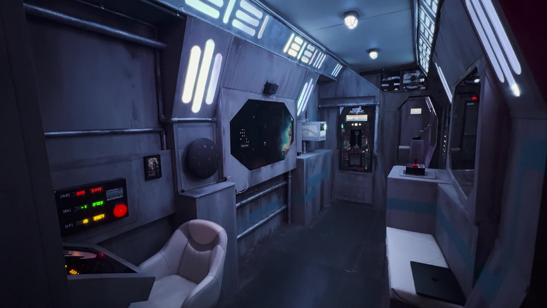 Wide interior view of the spaceship set with a padded chair, an octagonal window screen, illustrated wall panel, and glowing control panel reading ORION-V AUTOPILOT