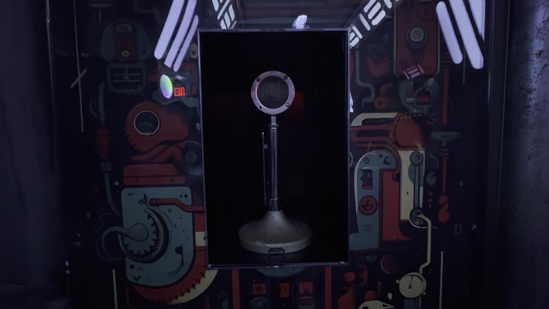 A vintage-style microphone mounted on a stand inside a recessed black alcove, set against an illustrated sci-fi mural wall