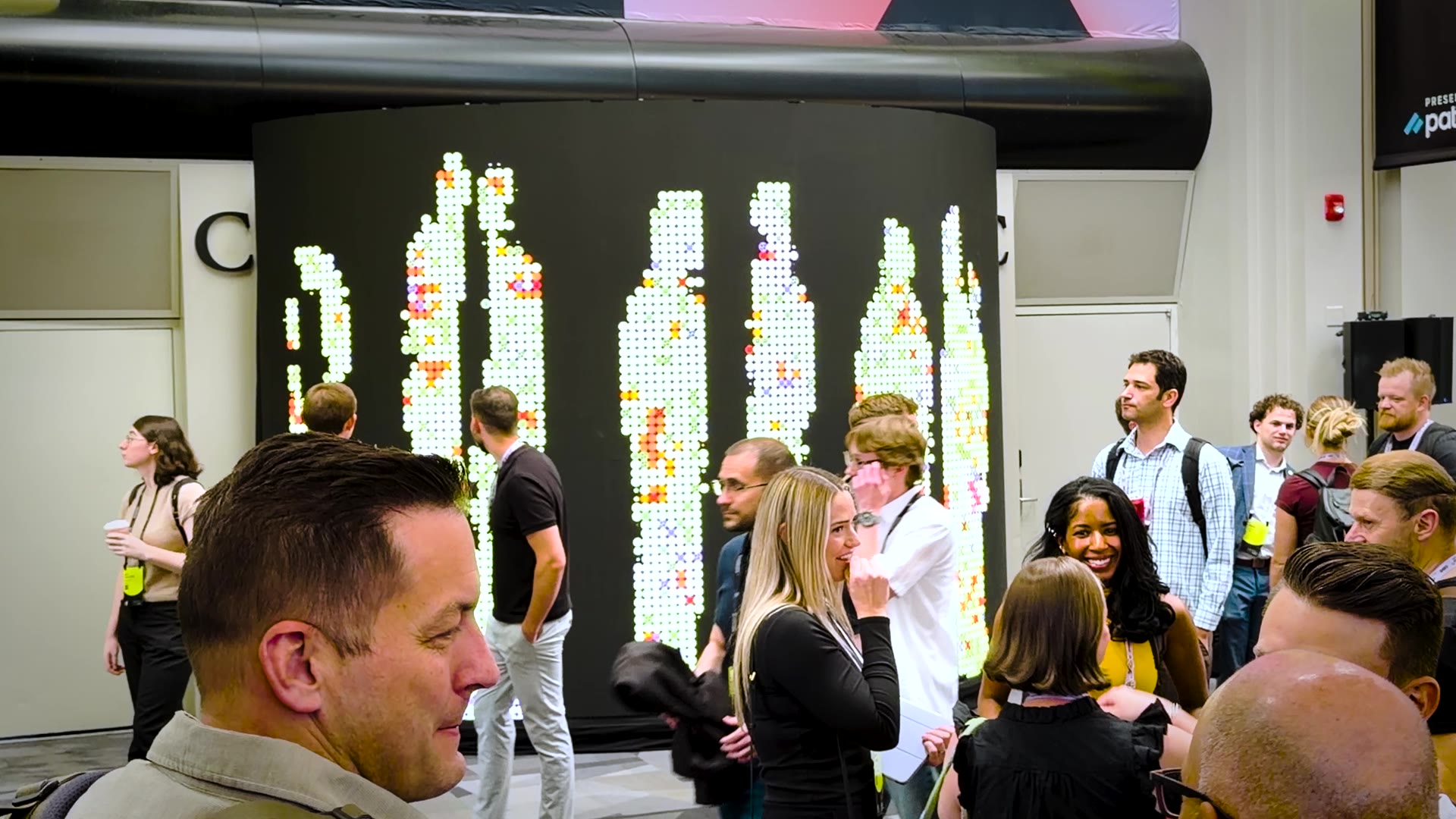 A group of six or more conference attendees standing in front of the wall, which displays six overlapping mirrored dot-grid figures at once