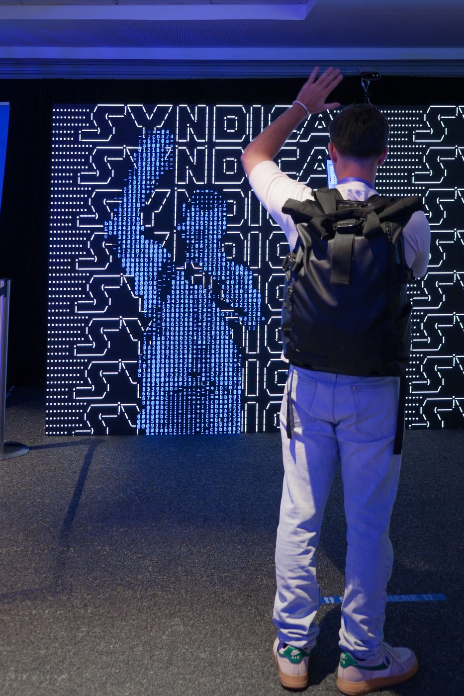 A visitor reaching up toward the wall, their arm resolved into the ASCII field in real time