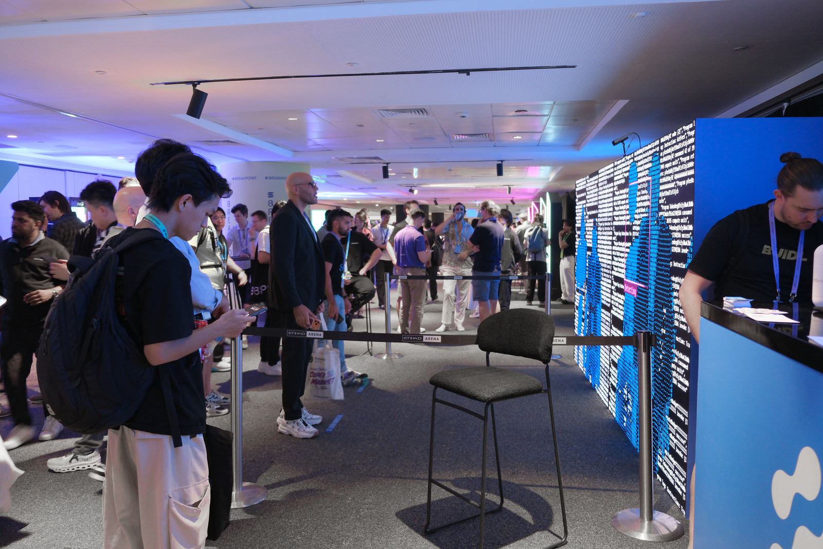 The Syndica stand on the Breakpoint conference floor, with a tracked visitor resolved into the LED wall at right