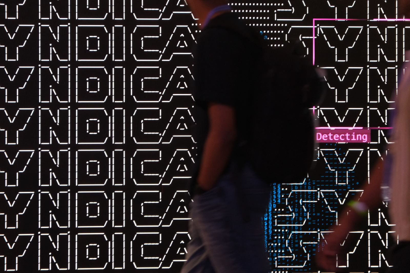 The Syndica wordmark tiled across the wall in ASCII characters