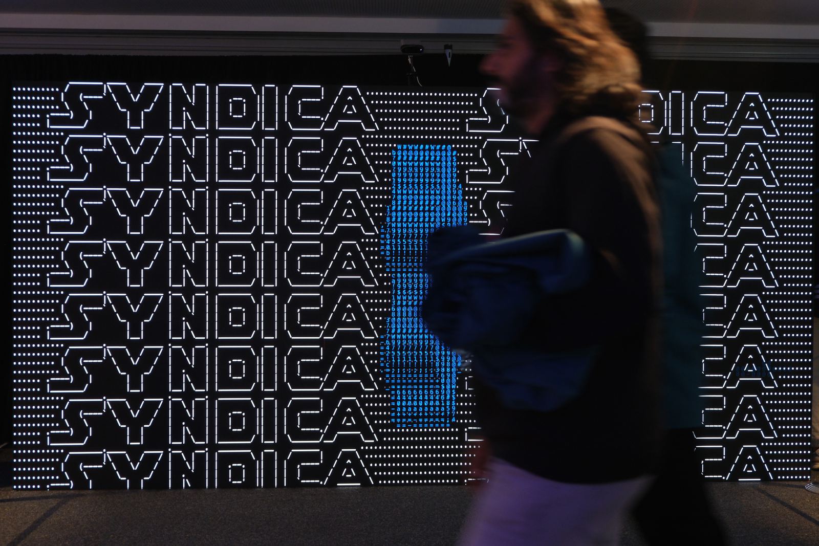 A visitor walking past the wall as the branded ASCII wordmark state plays